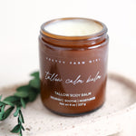 Pretty Farm Girl "Tallow Calm Balm" jar on a white stone surface with green botanical accent.
