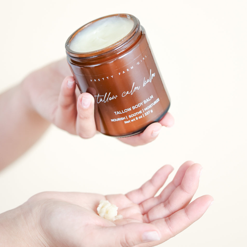 Pretty Farm Girl Tallow Calm Balm jar held above an open hand.