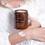 Pretty Farm Girl Tallow + Honey Tallow Body Balm jar held in hand on a soft white fabric background.