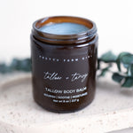 Pretty Farm Girl Tallow + Tansy Tallow Body Balm jar on a white stone surface with green botanical accent.