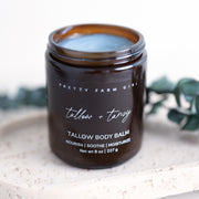 Pretty Farm Girl Tallow + Tansy Tallow Body Balm jar on a white stone surface with green botanical accent.