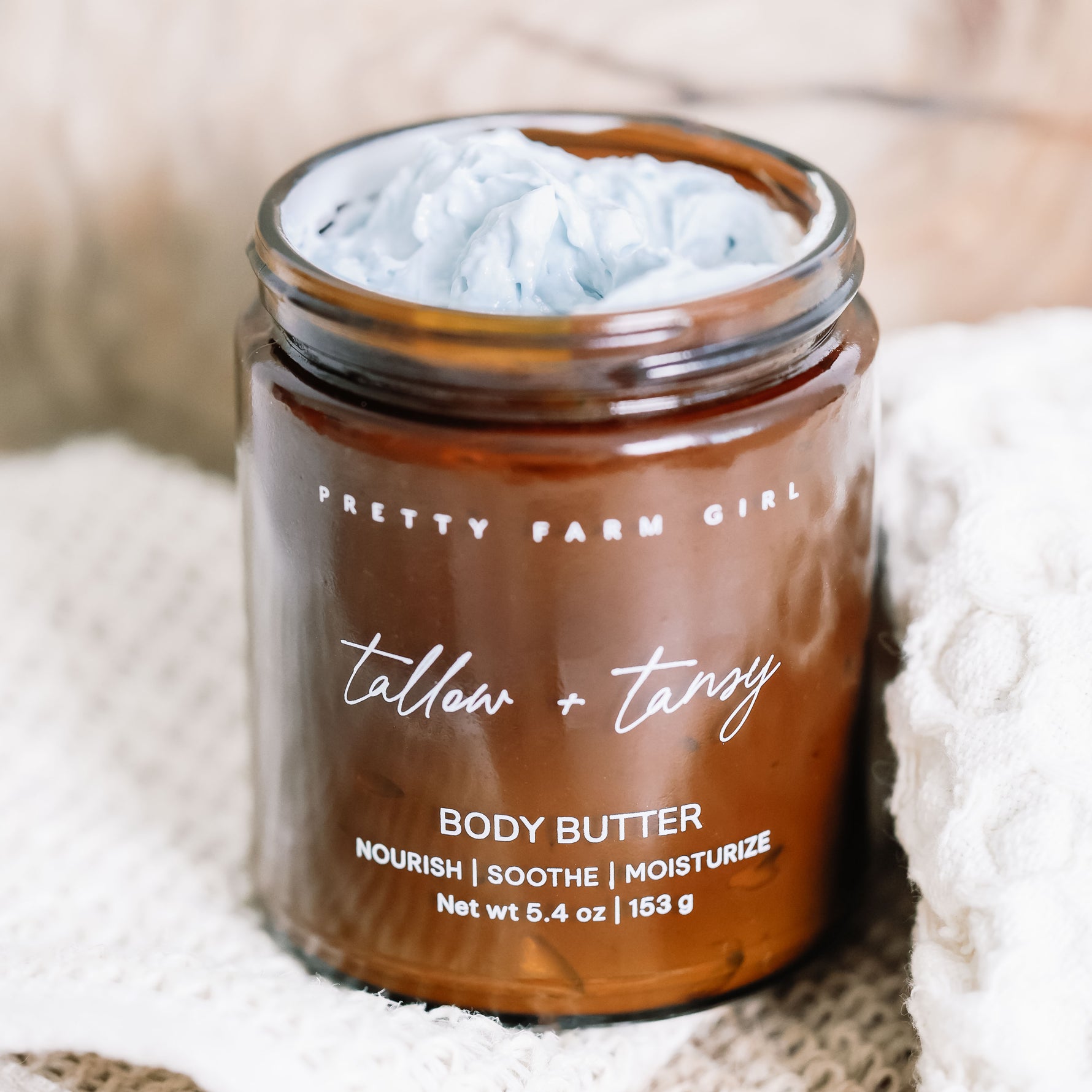 Jar of Tallow Tansy body butter opened showing the light blue whipped texture on a soft background