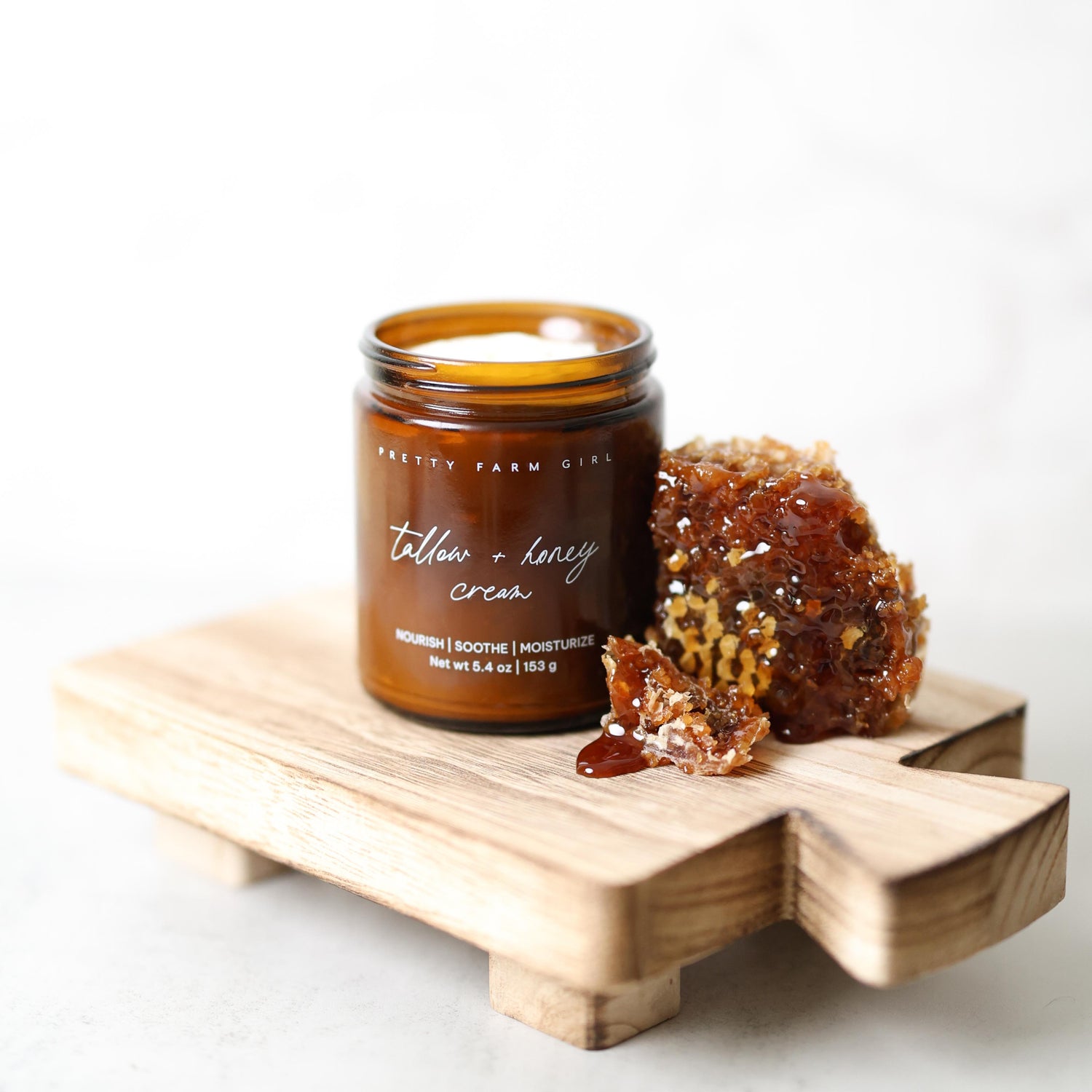 Jar of Pretty Farm Girl fragrance free tallow + honey cream on a wooden board with honeycomb next to it on a white background. 