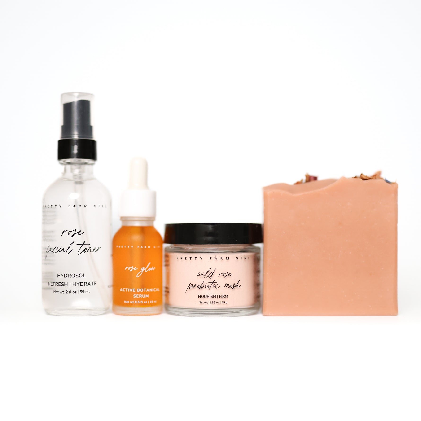 Set of natural products including Rose facial toner, rose glow serum, wild rose probiotic mask, and a pink wild rose soap bar on a white background.