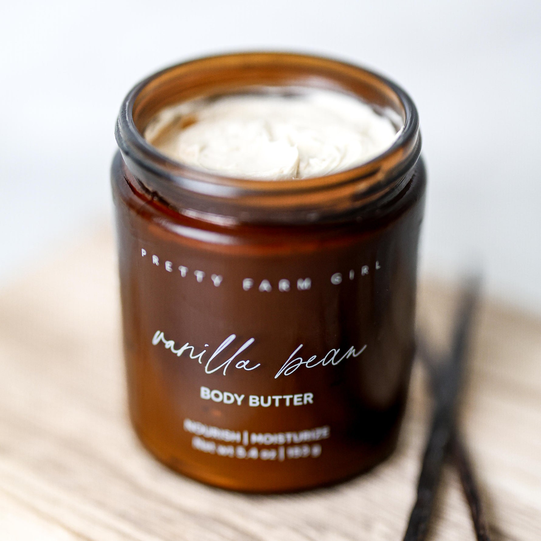 Jar of Pretty Farm Girl vanilla bean tallow body butter with out the lid on to show cream texture light surface.