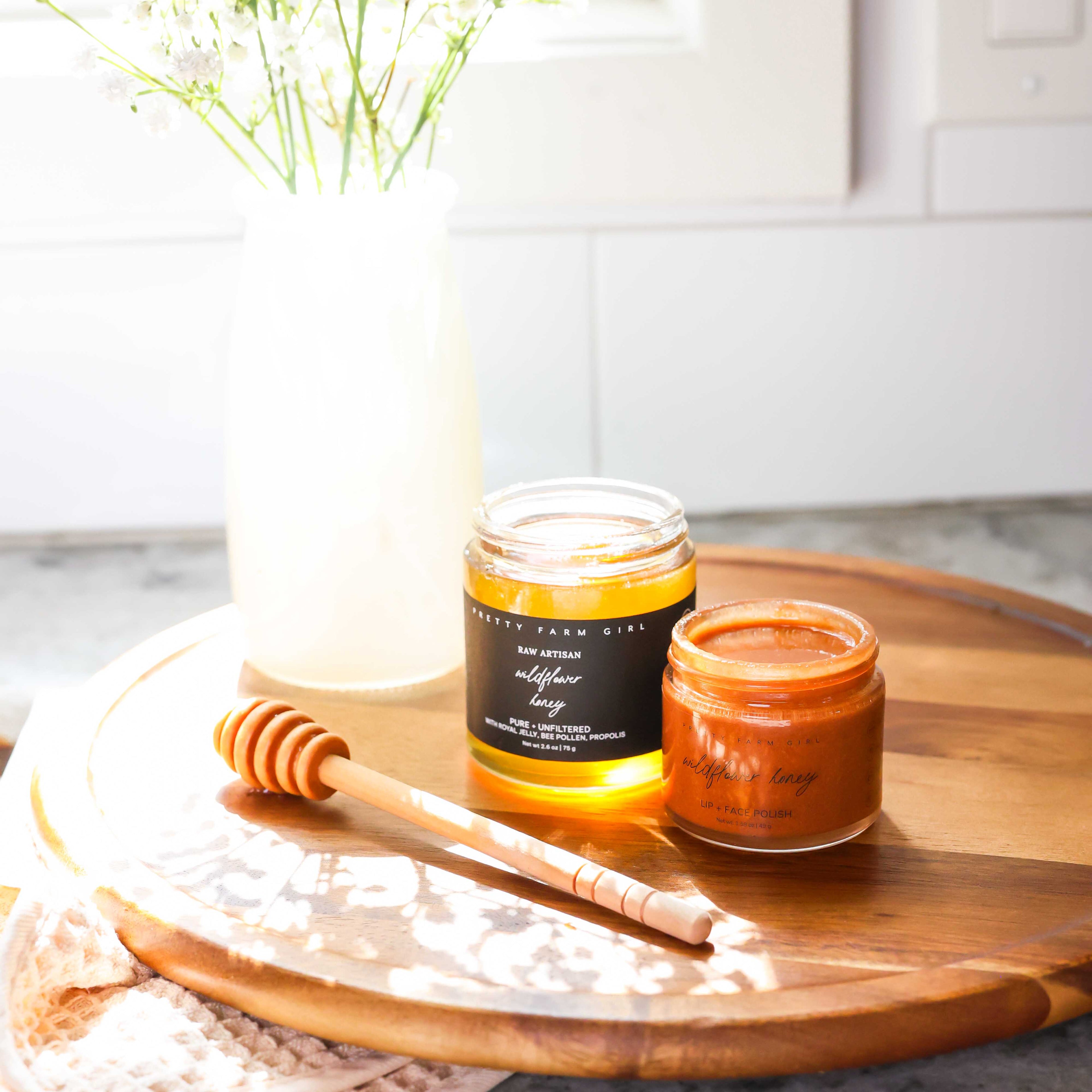 Two jars on a wooden cutting board. They are labelled raw artisan wildflower honey and wildflower honey lip and face polish.