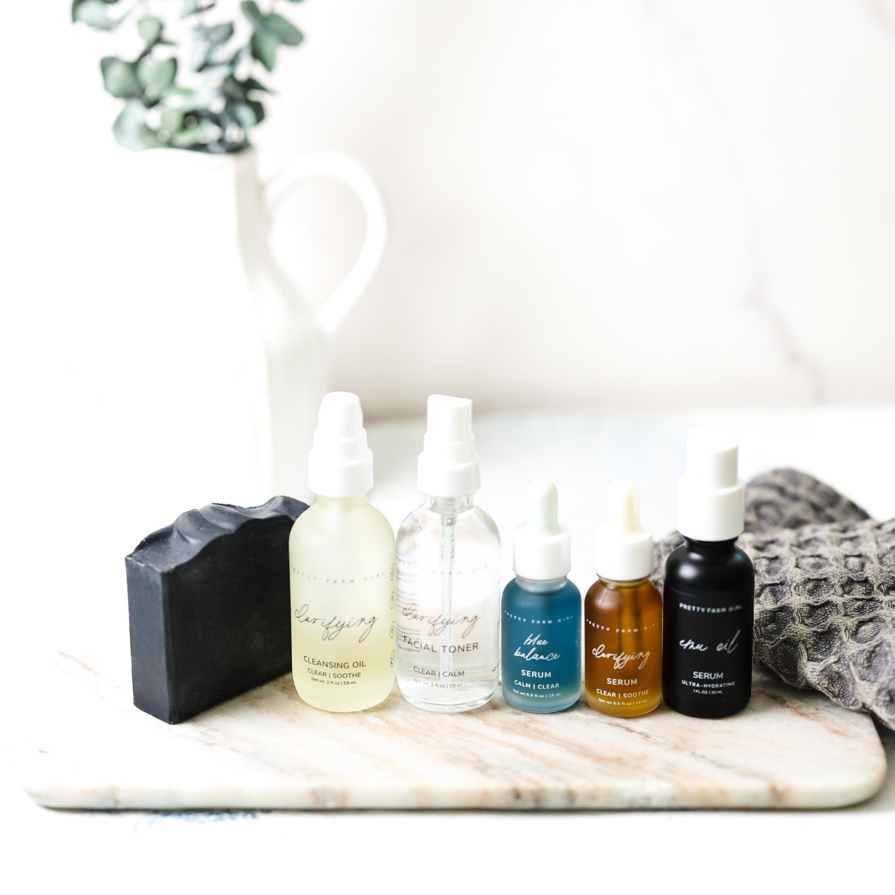 Set of skincare products on a marble surface with a white pitcher and plant in the background.