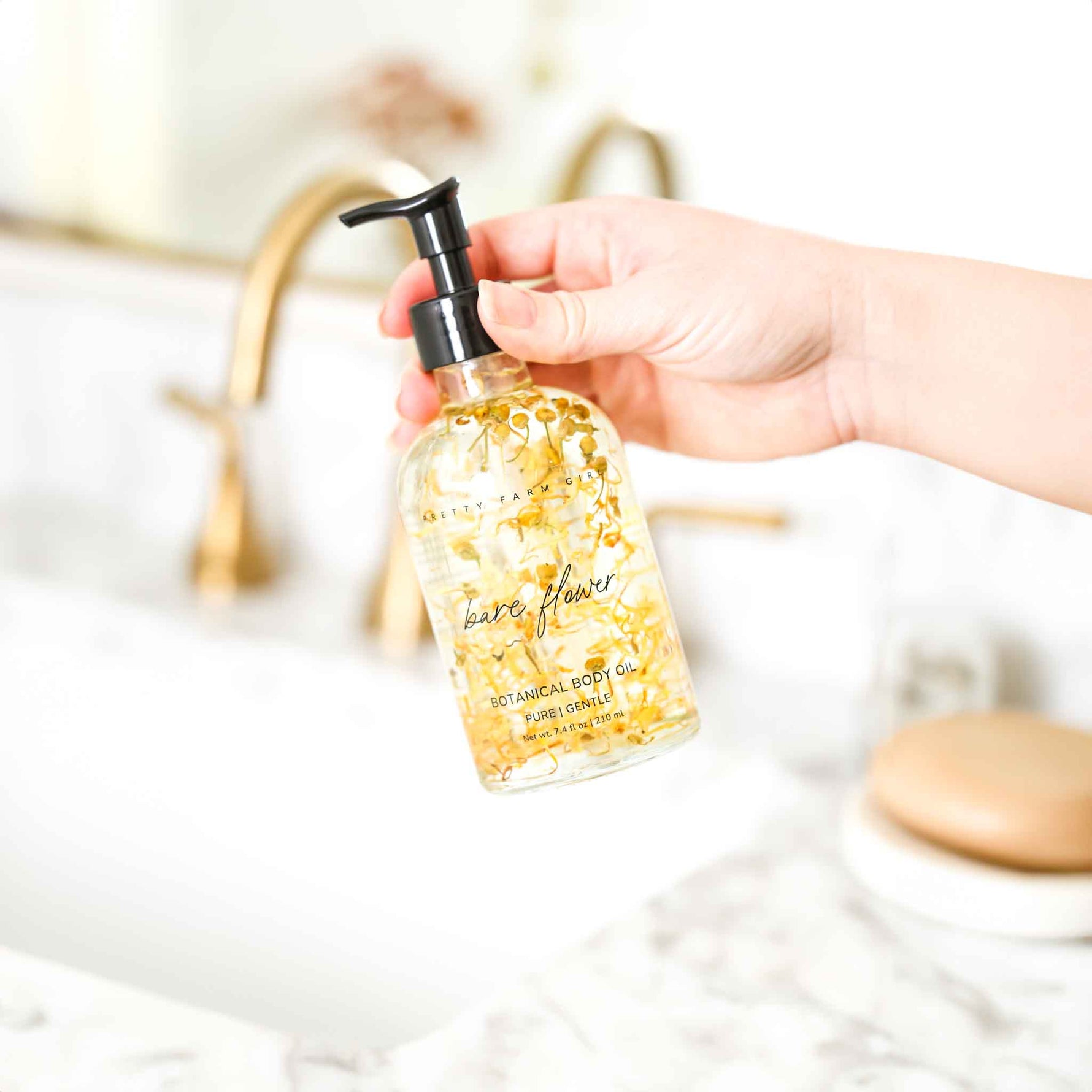 Hand holding a bottle of 'bare flowers' botanical body oil with a blurred bathroom background