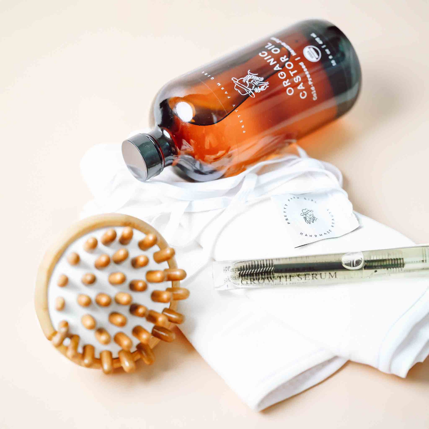 Bottle of organic castor oil bottle, castor oil cloth pack, bamboo scalp massage, and eyelash serum laid down on a light surface