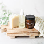 Skincare products including a bar of soap, cleansing oil, and cream on a wooden block with a white background.