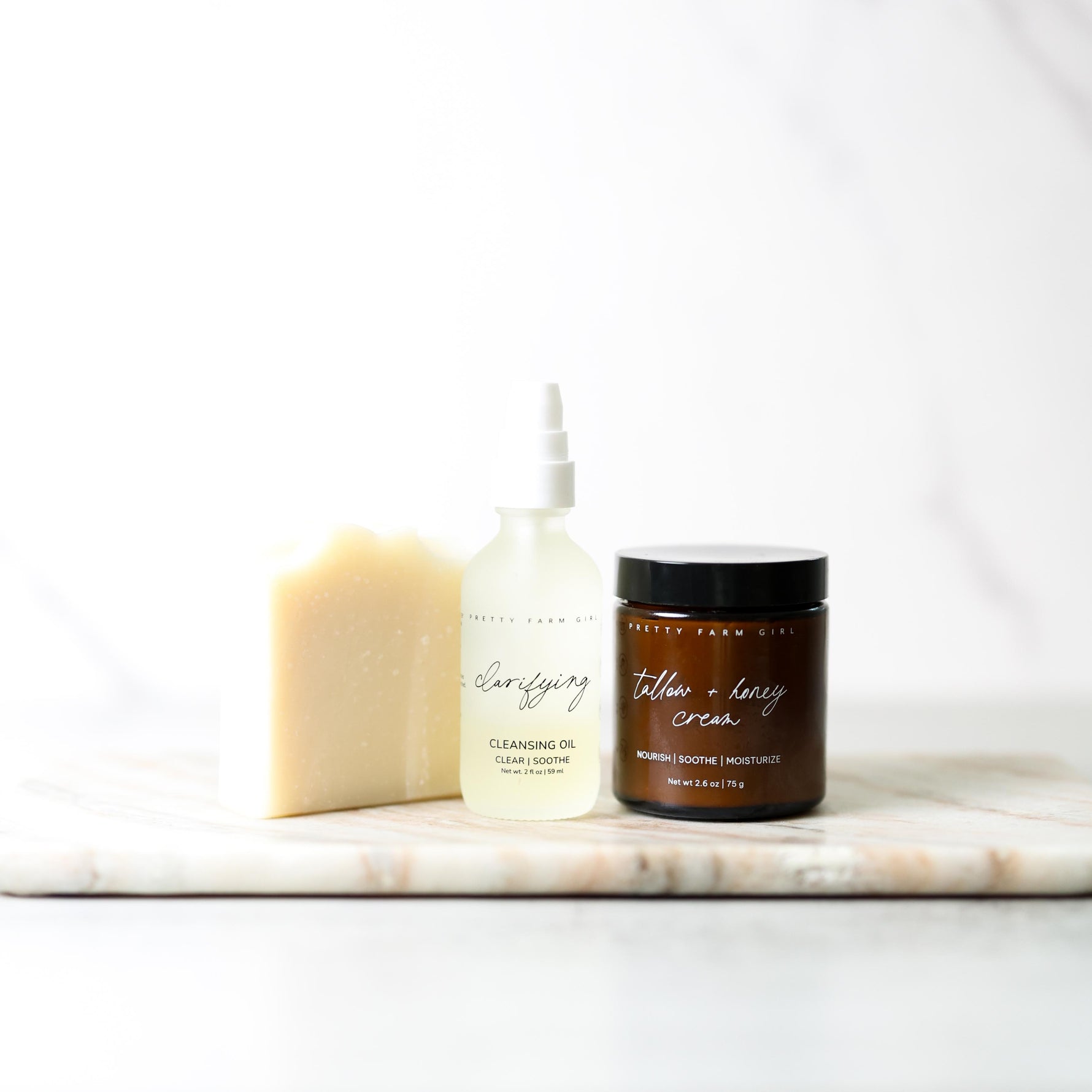 Skincare products including a bar of soap, cleansing oil, and cream on a marble surface with a white background.