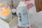 Hand holding a package of SEALD face tape with a candle and jars in the background