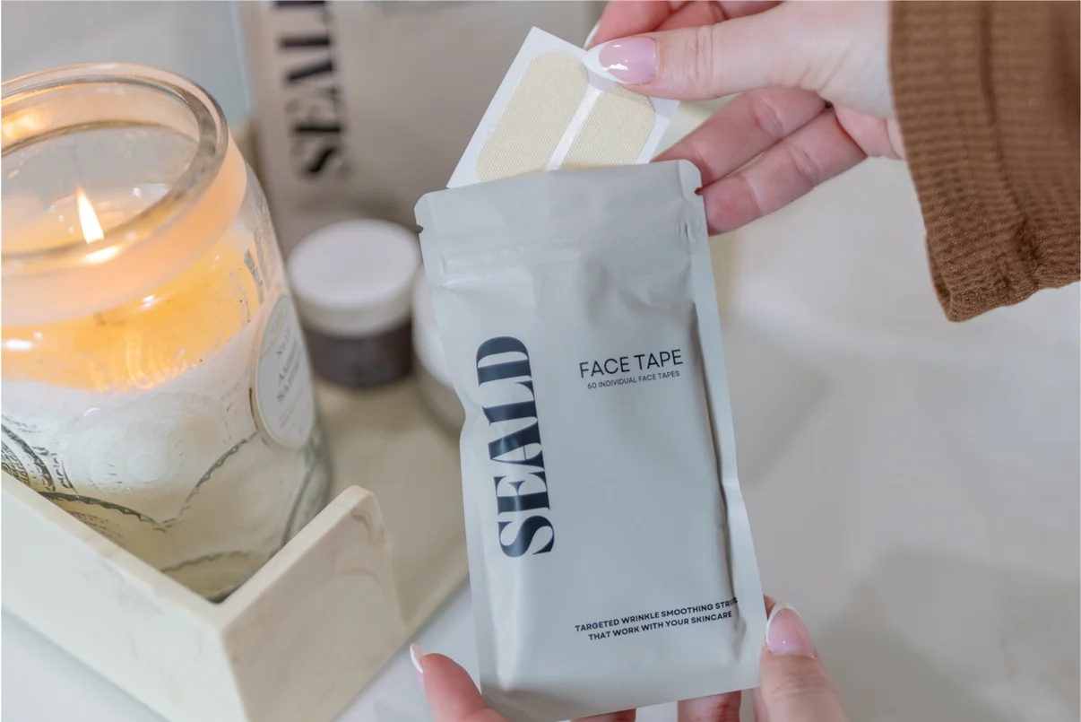 Hand holding a package of SEALD face tape with a candle and jars in the background