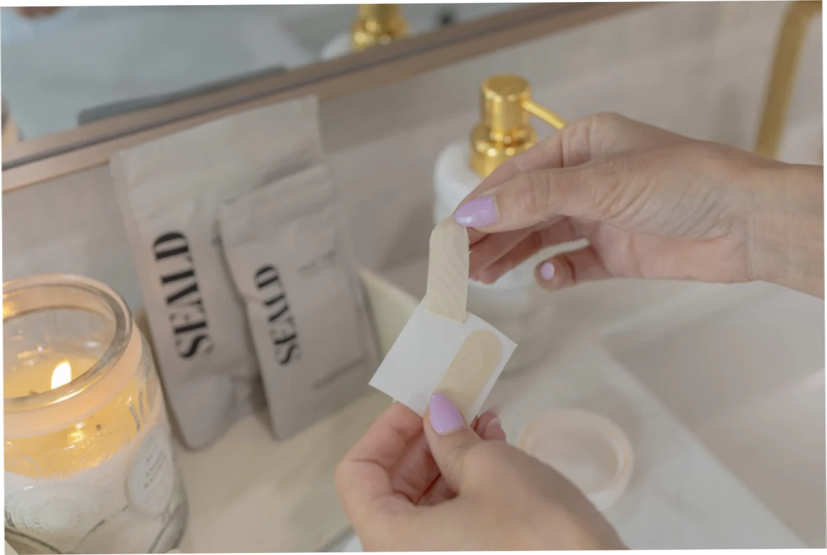 Person holding thin face tape over a sink with candles and books in the background