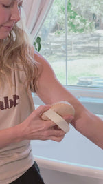 A multi media video of the founder, Jen, using a dry brush on her arm in her bathroom.
