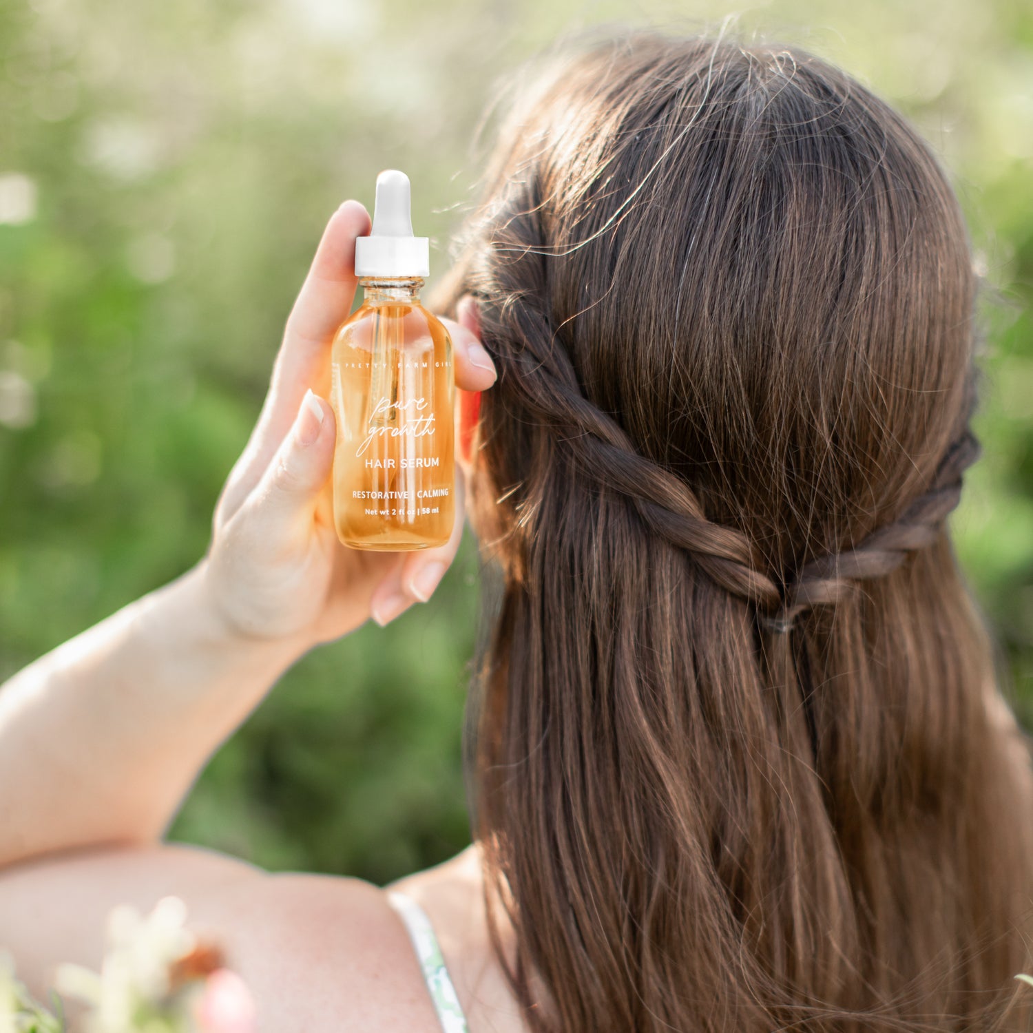 Pure Growth Hair Serum bottle held against long hair outdoors