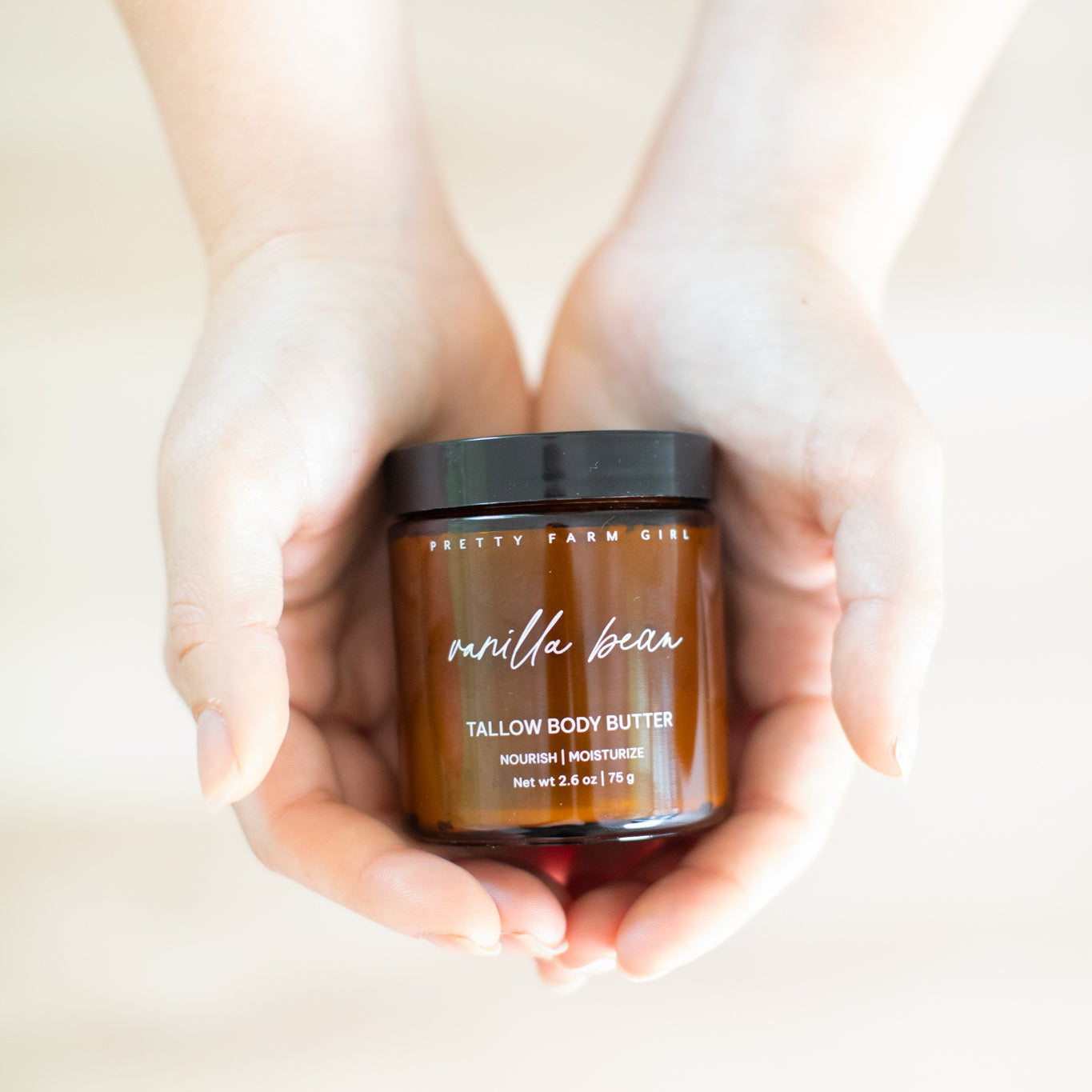 Jar of Pretty Farm Girl vanilla bean tallow body butter held in hands against a neutral background