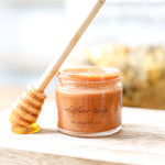 Jar of Wildflower Honey lip and face polish with a display honey dipper on a wooden surface