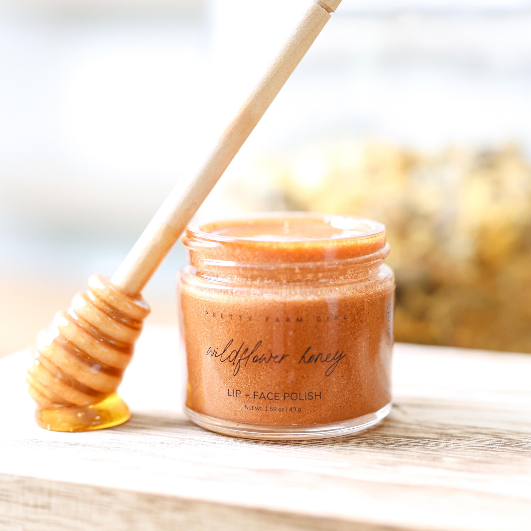 Jar of Wildflower Honey lip and face polish with a display honey dipper on a wooden surface