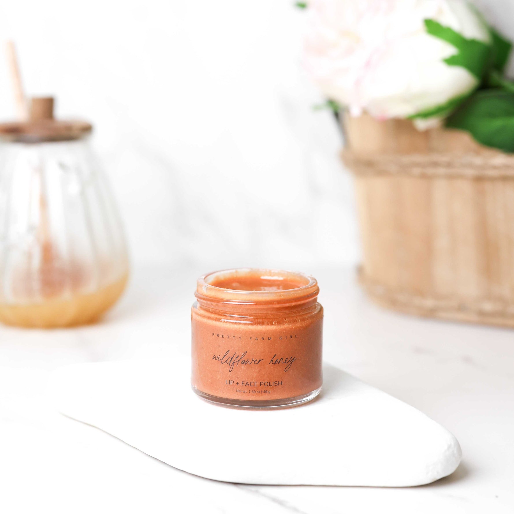 Jar of wildflower honey lip and face polish on a white surface with a blurred background